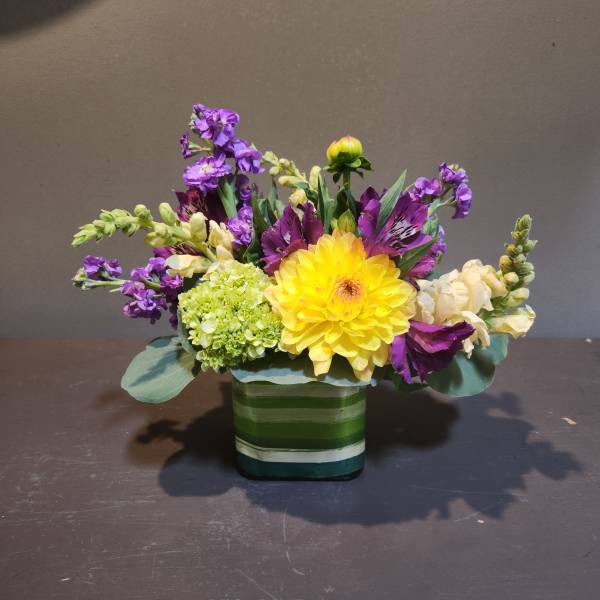 Yellow dahlia bouquet with purple and white flowers in a striped glass vase