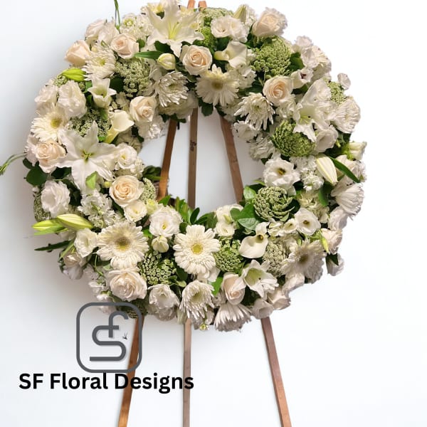 Large white and cream floral wreath with roses, lilies, and gerbera daisies on a wooden easel.