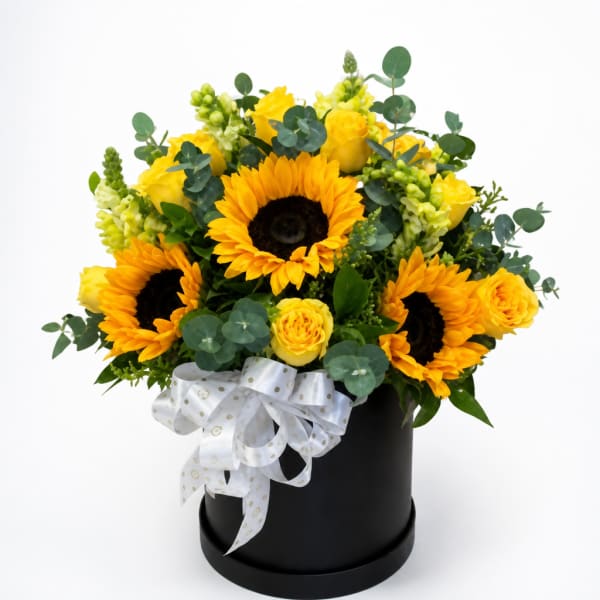 Yellow sunflowers and roses arranged in a black hatbox with a white ribbon