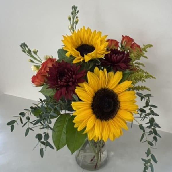 Sunflowers and burgundy flowers in a clear glass vase