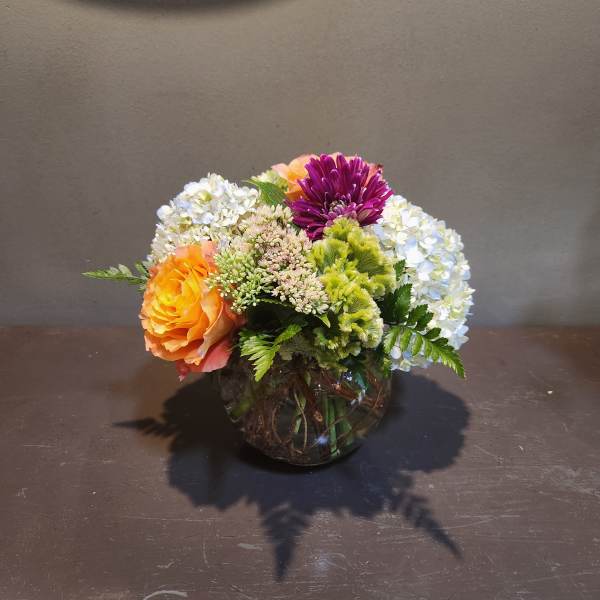 Mixed flower arrangement in a round glass vase with orange, purple, and white blooms