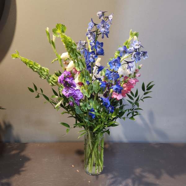 Tall mixed bouquet of blue, purple, pink, and white flowers in a clear glass vase