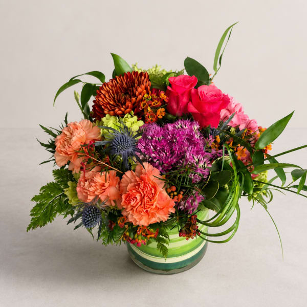 Mixed bouquet in a striped glass vase with pink roses and orange carnations