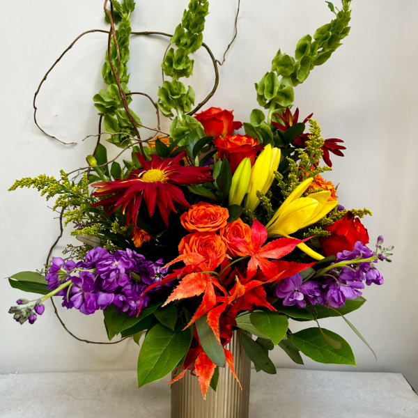 Colorful mixed bouquet in a ribbed vase with red, orange, yellow, and purple blooms