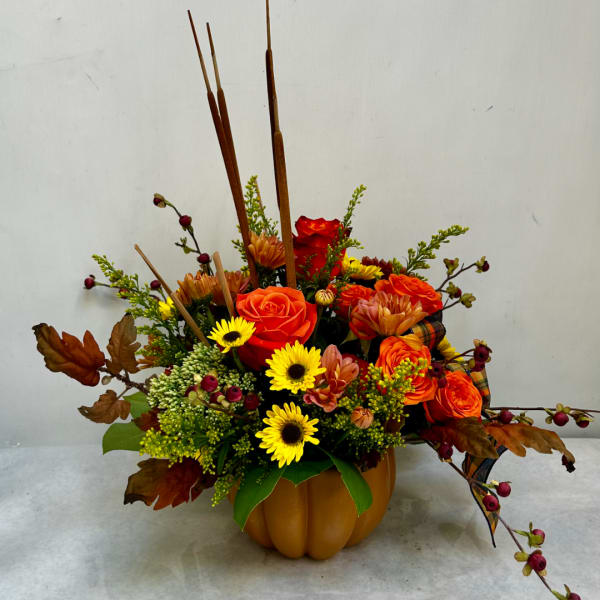 Autumn floral arrangement in a pumpkin-shaped container with orange and yellow blooms