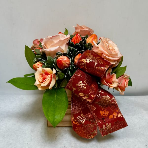 Peach roses arranged in a small wooden box with a red decorative ribbon