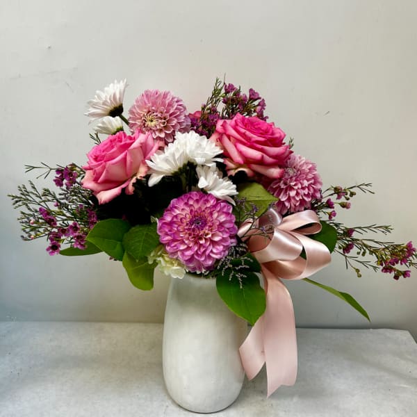 Pink roses and mixed blooms in a white vase with a pink ribbon