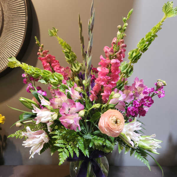 Mixed pink and white flowers in a glass vase with a purple ribbon