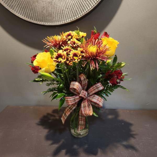 Bouquet of yellow roses and red chrysanthemums in a glass vase with a plaid ribbon