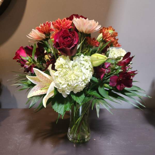 Mixed bouquet with roses, lilies, hydrangea, and daisies in a glass vase