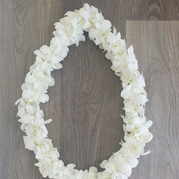White floral lei arranged in an oval shape on a wood floor