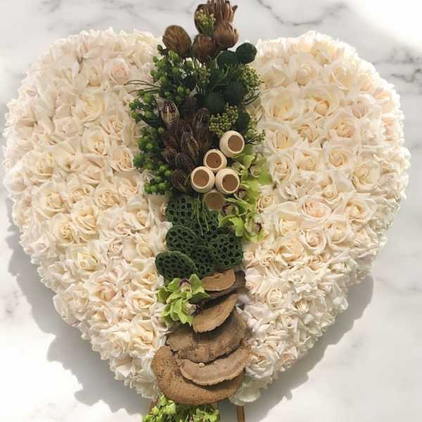 Heart-shaped floral arrangement of cream roses with a central green-and-brown decorative cascade
