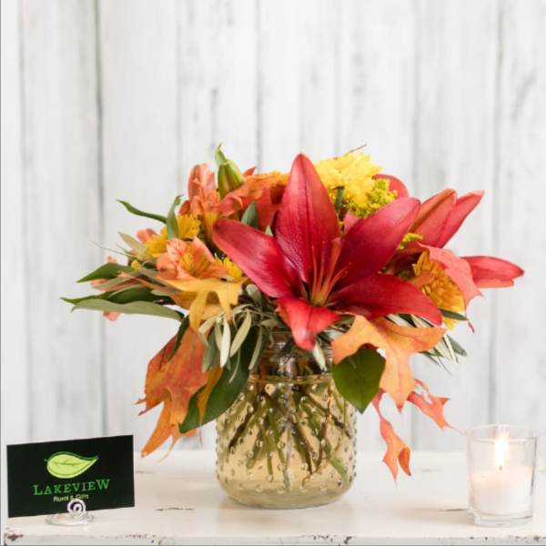 Autumn bouquet with red lilies and orange flowers in a gold glass vase