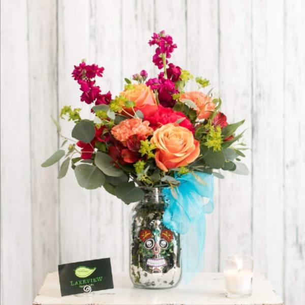 Bright mixed bouquet in a decorated glass jar vase with a blue ribbon.