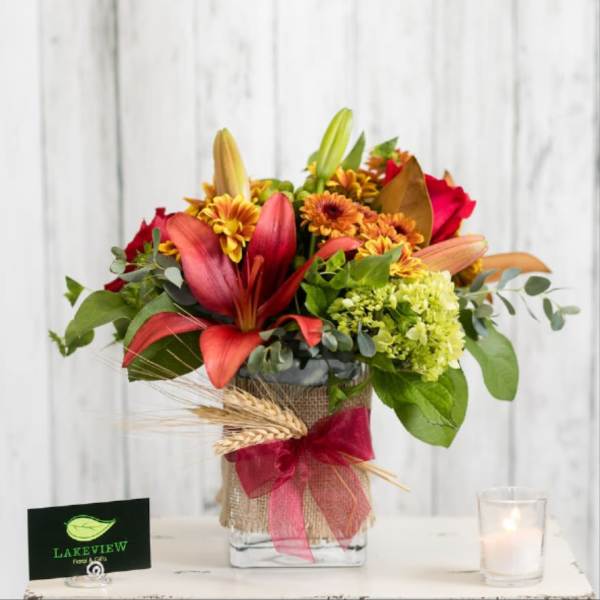Bouquet of red lilies, yellow mums, and green hydrangea in a glass vase