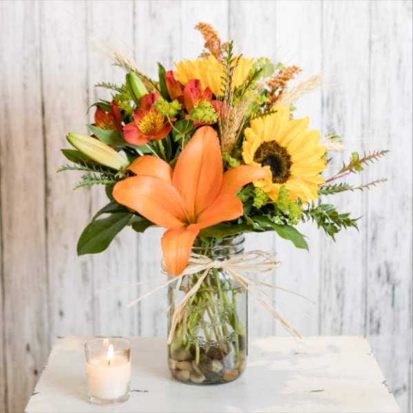 Orange lilies and sunflowers in a glass vase with a candle nearby.