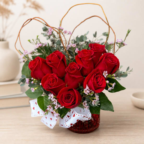 Red roses in a glass vase with a white heart ribbon