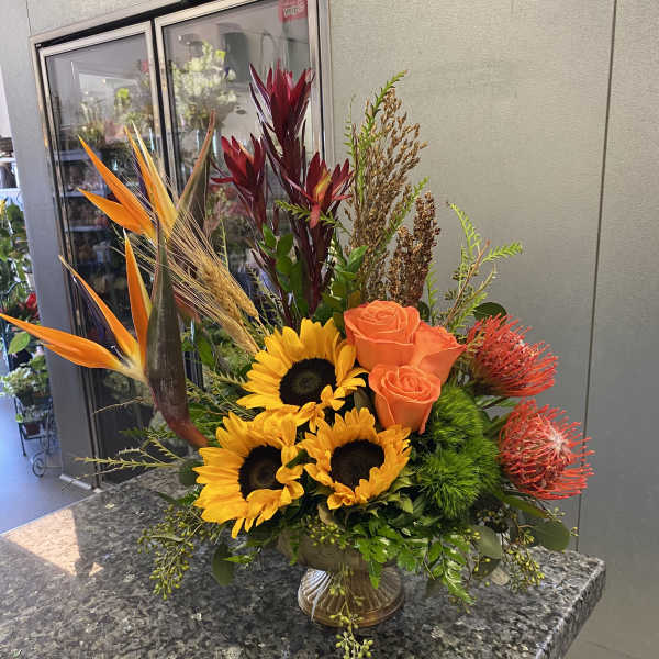 Tropical bouquet with sunflowers, orange roses, and bird of paradise in a vase