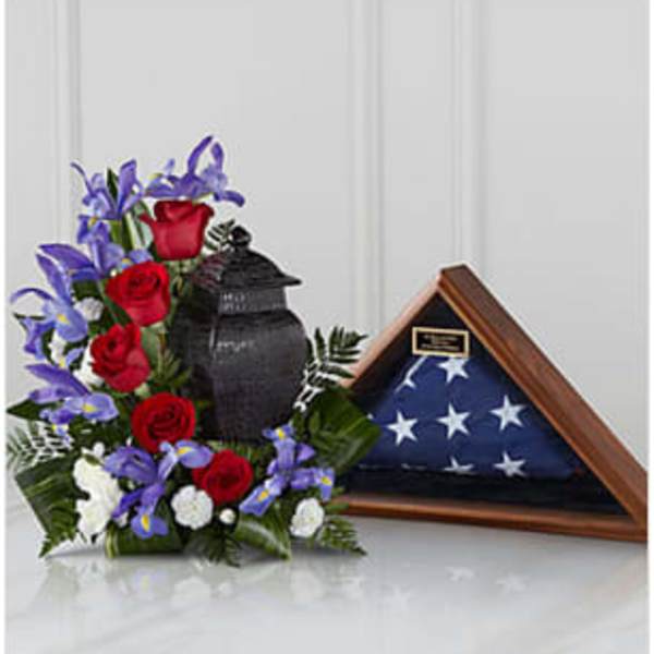 Red roses and purple flowers arranged beside a folded American flag in a display case