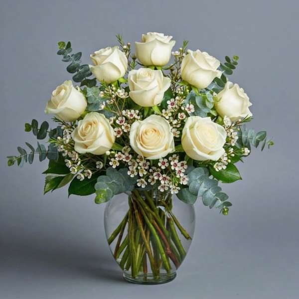 White roses arranged in a clear glass vase with small white filler flowers