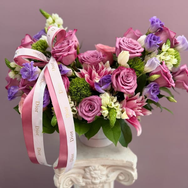 Pink and purple bouquet of roses and lilies in a white vase with ribbon