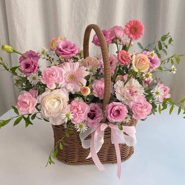 Pink and white flower arrangement in a wicker basket with ribbon