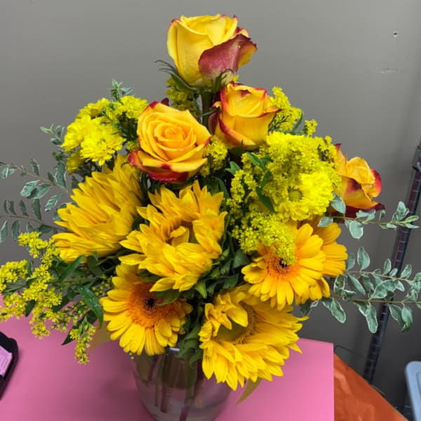 Yellow roses and sunflowers arranged in a glass vase