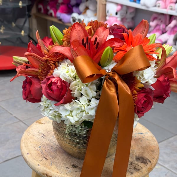 Red and orange flower arrangement in a gold vase with a satin ribbon