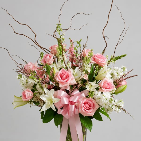Pink roses and white lilies in a glass vase with a pink ribbon
