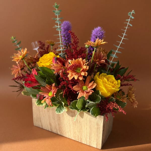 Mixed flower arrangement in a wooden box with yellow roses and orange daisies
