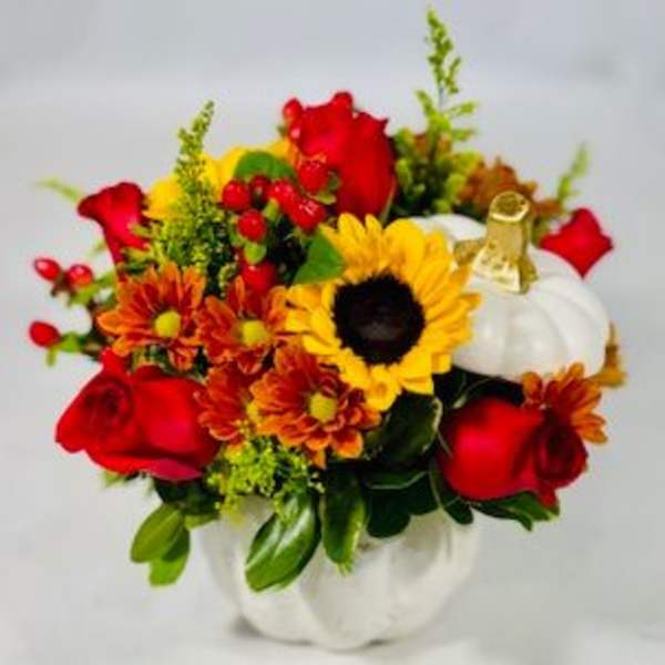 Bouquet of red roses, sunflowers, and orange mums in a white pumpkin container