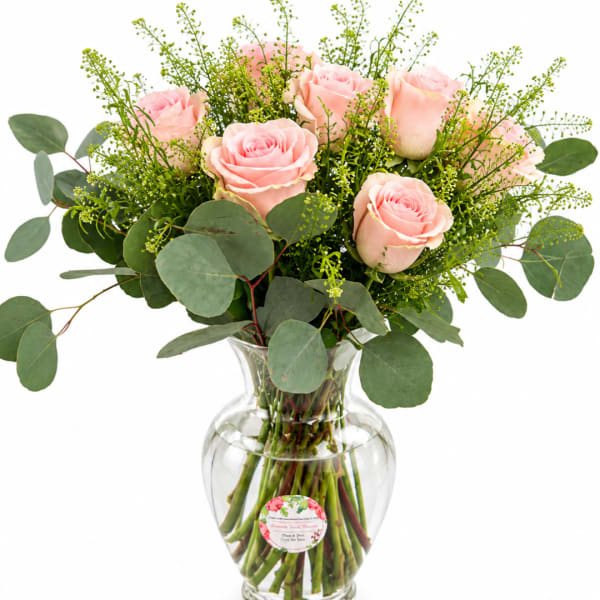 Pink roses arranged in a clear glass vase with eucalyptus foliage