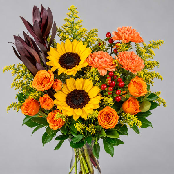 Bouquet of sunflowers, orange roses, and carnations in a clear glass vase