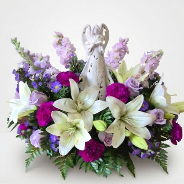White lilies and purple flowers arranged around a decorative angel figurine