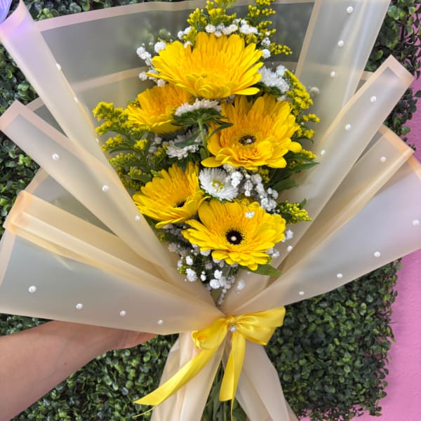 Yellow gerbera daisy bouquet wrapped in sheer beige paper with a yellow ribbon