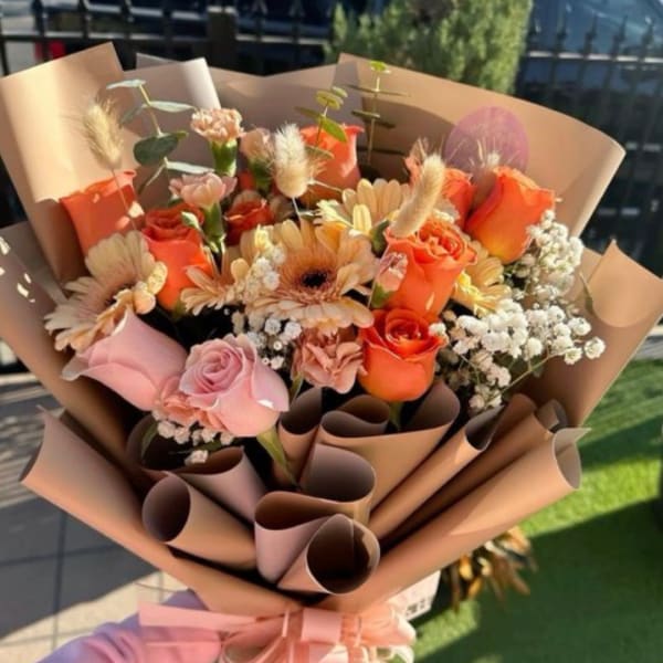Bouquet of orange and pink roses with daisies wrapped in tan paper