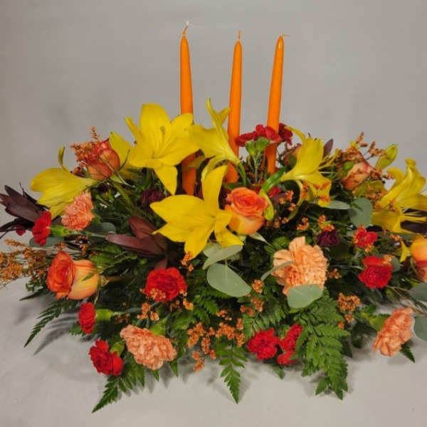 Low floral centerpiece with yellow lilies, orange roses, and orange candles