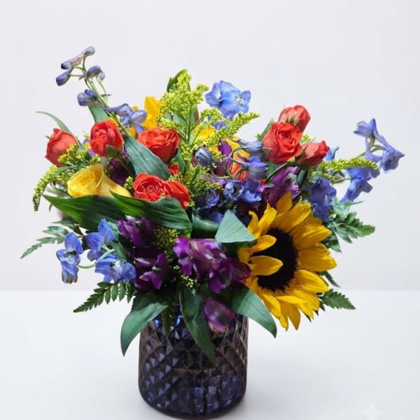 Colorful bouquet with roses, sunflowers, and blue flowers in a dark glass vase