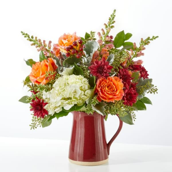 Orange and burgundy flowers arranged in a red pitcher vase