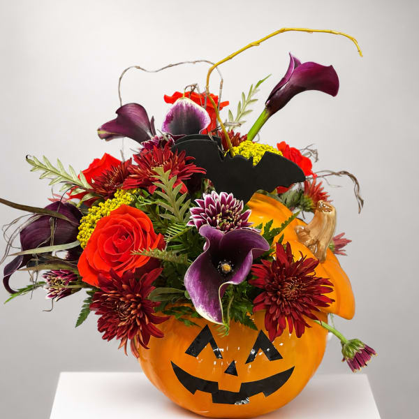 Halloween pumpkin container filled with purple calla lilies and red flowers