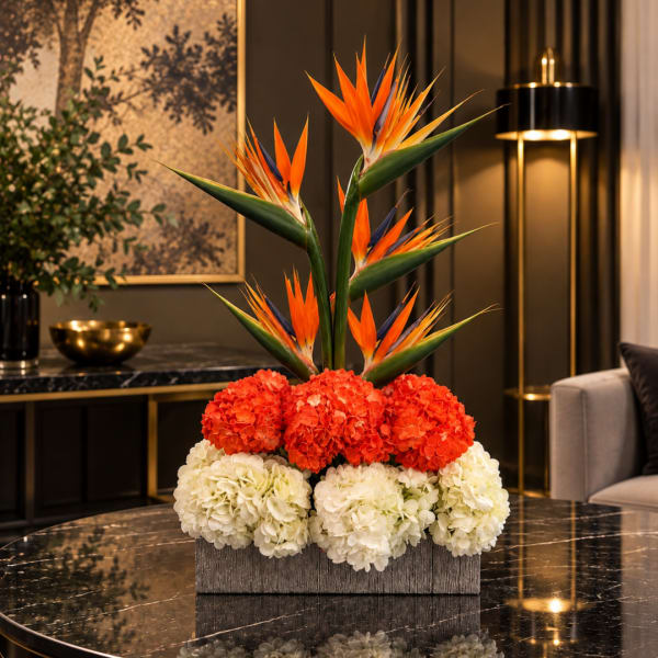 Tropical floral arrangement with orange bird-of-paradise and red and white blooms in a rectangular container
