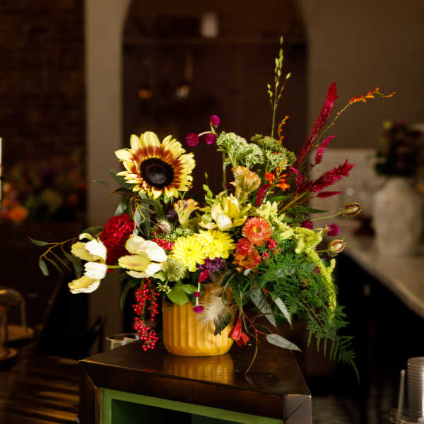 Colorful mixed flower arrangement in a yellow vase on a counter