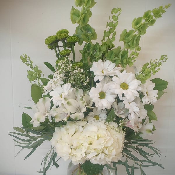White daisies and hydrangea in a glass vase with green accents