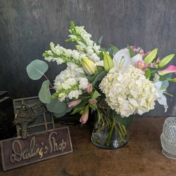 White lilies and hydrangeas in a glass vase with pink accents
