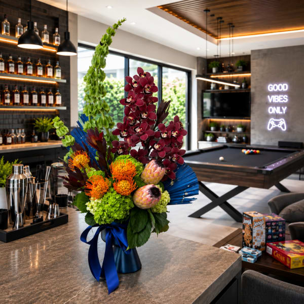 Tall tropical flower arrangement in a blue vase with a ribbon