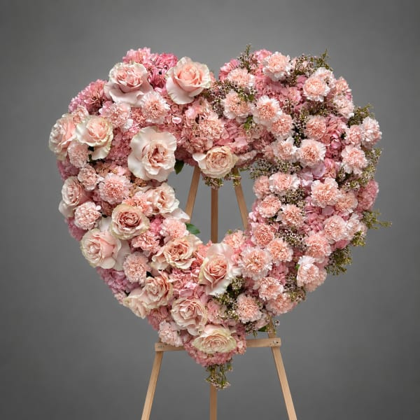 Heart-shaped pink floral wreath on a wooden easel