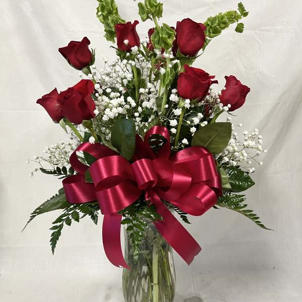 Red roses in a glass vase with baby's breath and a pink ribbon bow