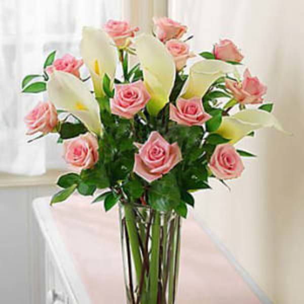 Pink roses and white calla lilies in a tall glass vase