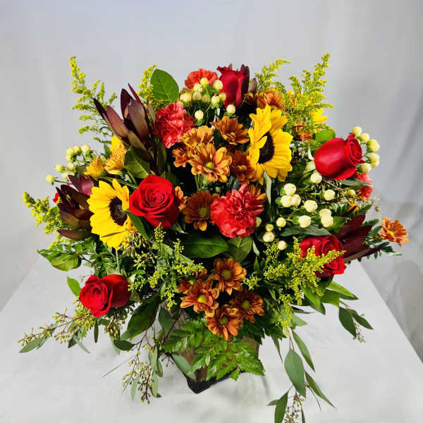 Mixed bouquet with red roses, sunflowers, and orange mums in a vase