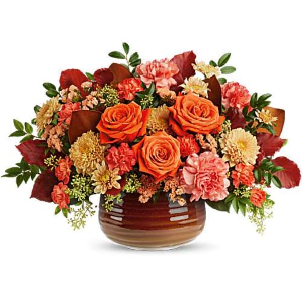 Orange roses and mixed fall flowers in a brown glass vase